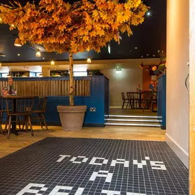 Zizzi - Glasgow Princes Square, vibrant interior with banquet seating and gallery views, and orange foliage creating an inviting atmosphere.