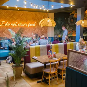 Zizzi Exeter, modern interior with vibrant neon decor and hanging ceiling decor and foliage, creating a warm dining room experience.