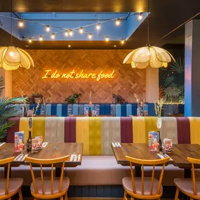 Zizzi Exeter, modern interior with vibrant neon decor and hanging ceiling decor and foliage, creating a warm dining room experience.