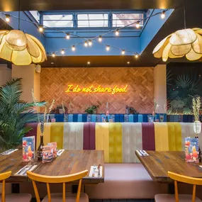 Zizzi Exeter, modern interior with vibrant neon decor and hanging ceiling decor and foliage, creating a warm dining room experience.