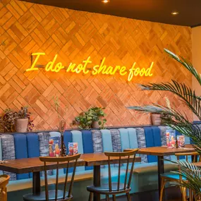 Zizzi Exeter, modern interior with vibrant neon decor and hanging ceiling decor and foliage, creating a warm dining room experience.