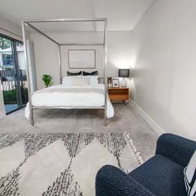 Model apartment bedroom with a bed, chair and rug, and patio door