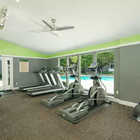 Fitness center with cardio equipment and windows overlooking a swimming pool