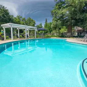 a large swimming pool with chairs and trees in the background