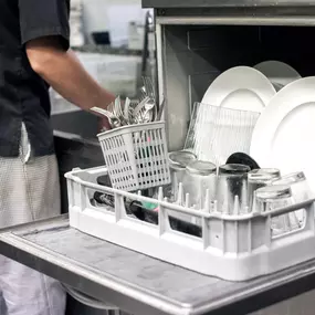 Kitchen hand with an open dishwasher filled with clean white plates in a restaurant kitchen in a catering and hygiene concept