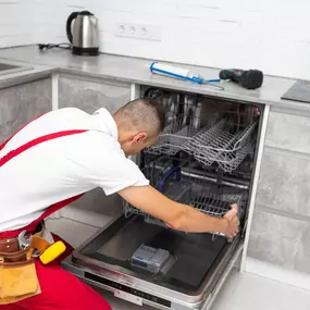 The dishwasher open with a man who is putting the bottom tray back into it