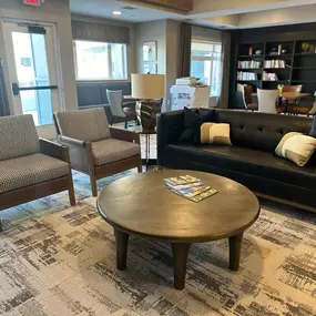 This cozy lounge area at Saint Therese of Corcoran features comfortable seating, a coffee table, and a bookshelf filled with books.