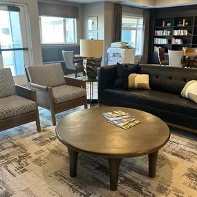 This cozy lounge area at Saint Therese of Corcoran features comfortable seating, a coffee table, and a bookshelf filled with books.