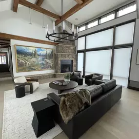 Enhance your modern rustic great room with custom window shades from GrandView Blinds & Designs. These light-filtering shades manage natural light from the large windows, complementing the vaulted ceilings, wood beams, and stone fireplace.