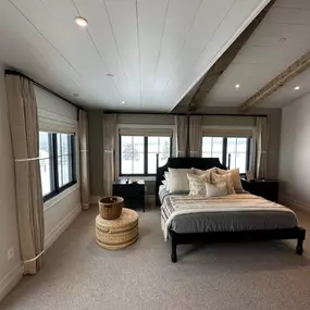 Create a cozy and sophisticated bedroom retreat with layered window treatments from GrandView Blinds & Designs. Combining functional Roman shades with decorative drapery panels adds texture, warmth, and versatile light control that complements modern rustic decor.