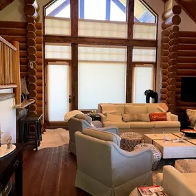 Outfit your log cabin's unique windows with custom cellular shades from GrandView Blinds & Designs. This rustic great room showcases shades expertly fitted to large, multi-sectioned, and angled windows, providing light control and energy efficiency while complementing the log structure.