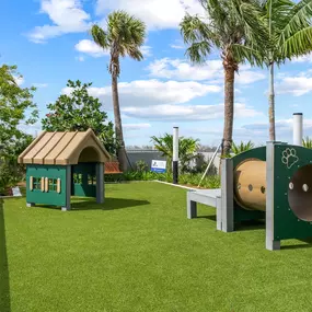 A pet-friendly space designed with a playground for dogs, featuring colorful structures like a doghouse and tunnel, surrounded by lush greenery.