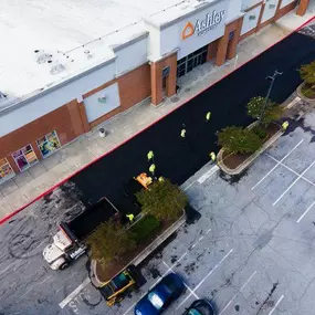 Aerial shot of Blackjack Paving contractors laying fresh asphalt in a parking lot outside of an Ashley HomeStore