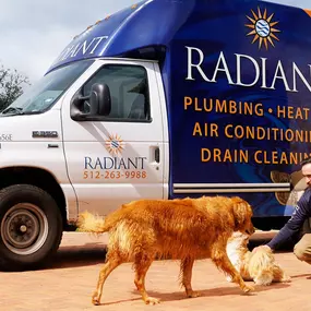 A Radiant Plumbing and Air Conditioning - Austin technician plays with a golden retriever next to the company truck