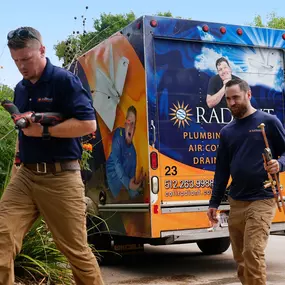 Two Radiant Austin technicians walk with tools from the truck