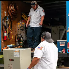 Two HVAC technicians at 72 Degrees Texas unload a system from their truck