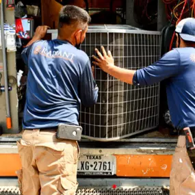 Two Radiant San Antonio HVAC technicians removing an AC unit from the truck