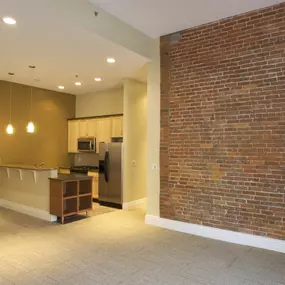 an empty living room with a brick wall and a kitchen at The Granite Works Apartments , New York 14202