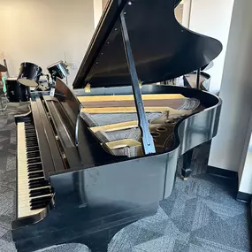 This image provides a close-up view of a grand piano in the Brock Family Music showroom. The open lid reveals the detailed construction of the strings and interior, emphasizing the craftsmanship and quality of the instrument.