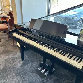 This image showcases a polished black Kawai digital piano, positioned near a large window that floods the space with natural light. The piano’s sleek, modern design is complemented by its built-in music stand and pedals, making it ideal for students and home use.