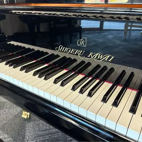 This close-up image captures the keyboard of a Shigeru Kawai grand piano, emphasizing the luxurious branding and precise craftsmanship. The polished black finish adds elegance, while the reflection highlights the piano’s pristine condition.