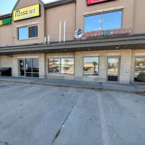 This photo shows the exterior of Brock Family Music, located in a convenient retail center. The storefront features large windows displaying instruments and the company’s signage, making it easily recognizable.