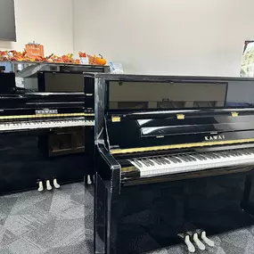 This photo features two polished black Kawai upright pianos displayed side by side in the Brock Family Music showroom. The sleek, reflective finishes and compact designs make them ideal for customers looking for space-saving instruments without compromising on quality or tone.