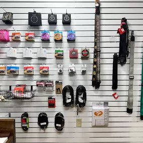 This image shows a neatly organized wall of guitar accessories at Brock Family Music. The display includes guitar strings, straps, cables, capos, and other essentials, all arranged on a slat wall for easy browsing.