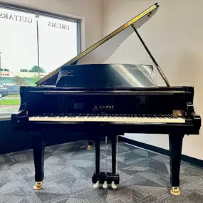 This image features a polished black Kawai baby grand piano displayed in a bright and modern showroom. The open lid showcases the craftsmanship, while the piano's compact size makes it an ideal choice for smaller spaces.