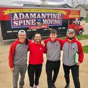 Four Adamantine Spine Moving employees posing cheerfully in front of a branded moving truck.