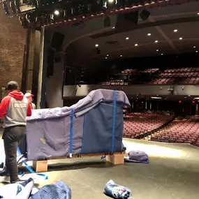 Movers handling a large object on a theater stage.