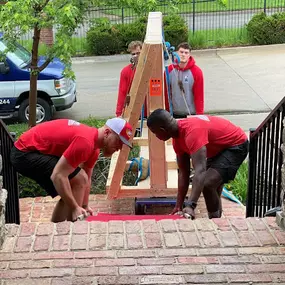 Movers carefully maneuvering a large item up brick stairs.