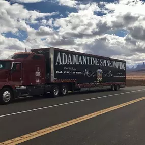 Adamantine Spine Moving semi-truck parked on a scenic desert highway.