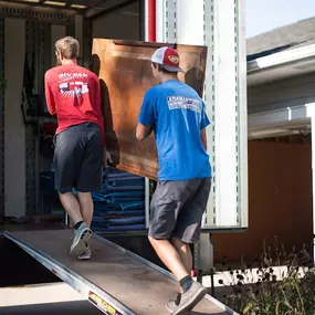 Movers unloading furniture into a home from a truck ramp.