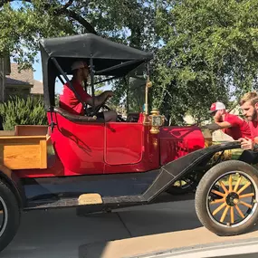 Team members pushing an antique red car into the moving truck.