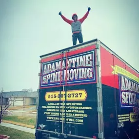 A mover standing triumphantly on top of an Adamantine Spine Moving truck.