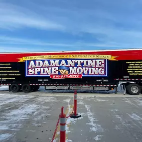 A long Adamantine Spine Moving semi-truck parked in a lot on a snowy day.