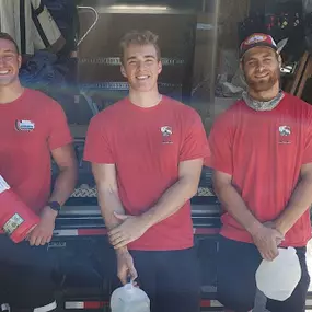 Three movers in red shirts standing at the back of an open moving truck.