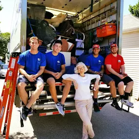 A happy customer posing with movers sitting on the edge of an open moving truck.