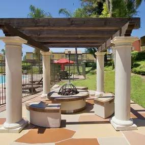a patio with a fire pit and a pergola overlooking a swimming pool