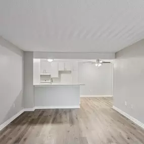 an empty living room and kitchen with white walls and wood flooring