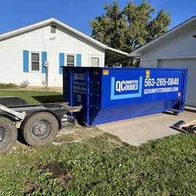 A QC Dumpster Dudes dumpster parked in a residential driveway, ready for cleanup or renovation projects.