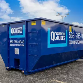 A blue QC Dumpster Dudes dumpster placed in an empty parking lot, ready for use in large-scale cleanouts or construction jobs.