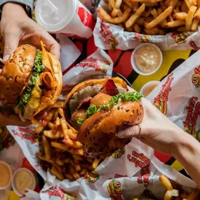 Close up of two people holding their burgers at Taystee's