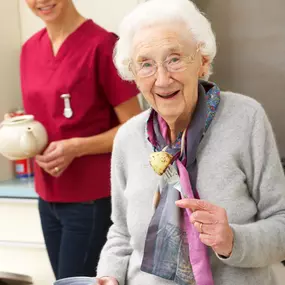 Senior woman with carer eating meal at home smiling at camera