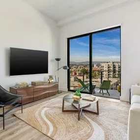 A living room with a black chair, a white sofa, a wooden coffee table, and a large window with a view of the city.