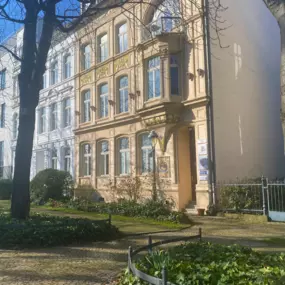 Ein charmantes historisches Gebäude umgeben von einem gepflegten Garten, das die harmonische Umgebung der Osteopathie-Praxis am Schloss Bonn unterstreicht.