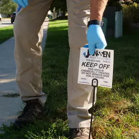 Janssen Pest Solutions technician installing a warning sign to Keep Off this area after pest treatment.