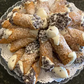 A plate of fresh cannoli desserts filled with cream and topped with powdered sugar, prepared by Cranberry Hills Eatery & Catering for catering events and dessert lovers.