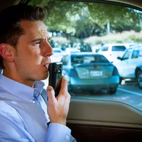 A male driver provides a breath sample using the Draeger Interlock 7000 before starting the vehicle.
